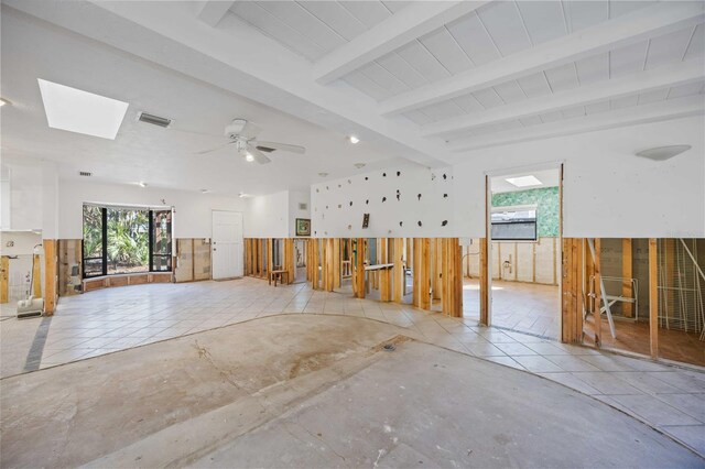 empty room featuring beamed ceiling, ceiling fan, wooden walls, and a skylight