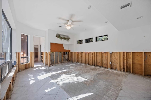 tiled empty room featuring ceiling fan and wood walls