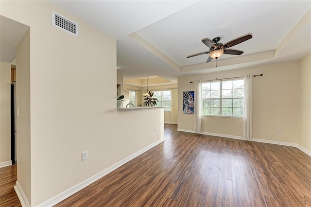 empty room with dark hardwood / wood-style flooring, a raised ceiling, and ceiling fan