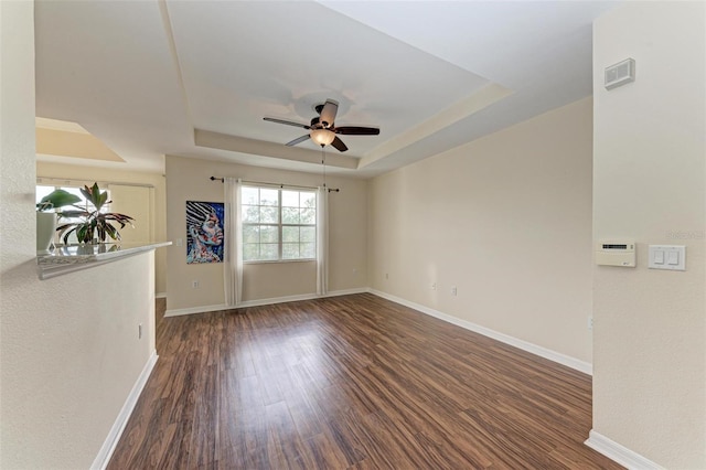 empty room with dark hardwood / wood-style floors, a raised ceiling, and ceiling fan