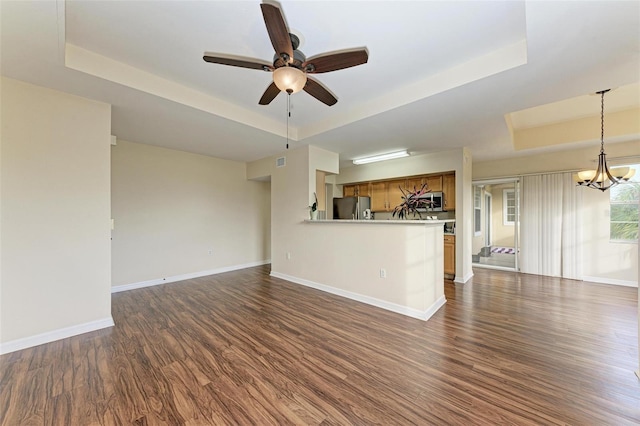 unfurnished living room with ceiling fan with notable chandelier, dark hardwood / wood-style flooring, and a raised ceiling