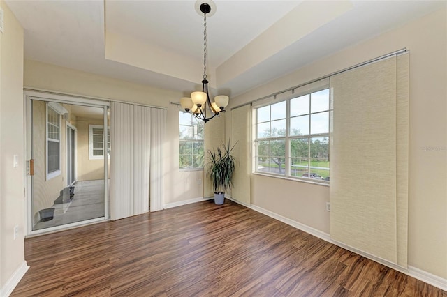 unfurnished dining area featuring dark hardwood / wood-style floors, a tray ceiling, and a chandelier