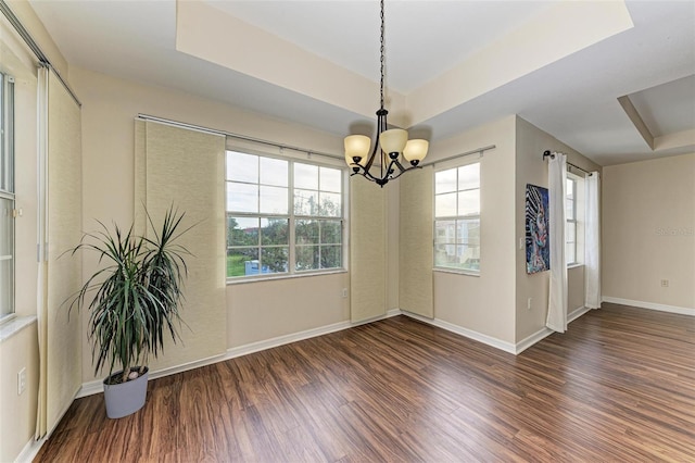 unfurnished dining area with a raised ceiling, dark hardwood / wood-style flooring, and a chandelier