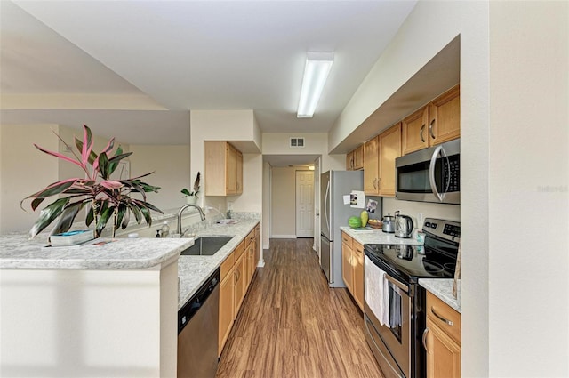 kitchen with sink, stainless steel appliances, light stone counters, kitchen peninsula, and light wood-type flooring