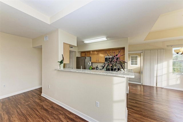 kitchen featuring kitchen peninsula, stainless steel fridge, light stone countertops, and dark hardwood / wood-style floors