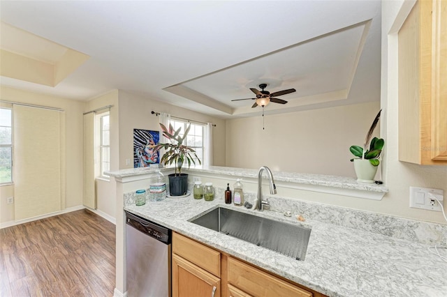 kitchen with light stone countertops, a tray ceiling, sink, hardwood / wood-style flooring, and dishwasher