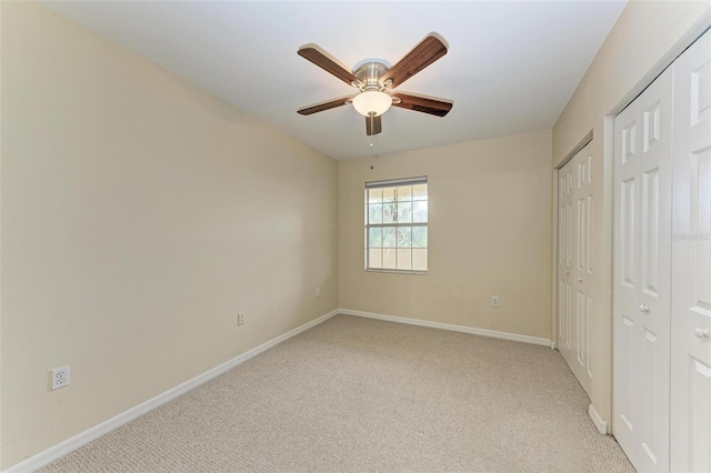 unfurnished bedroom featuring ceiling fan, light carpet, and multiple closets