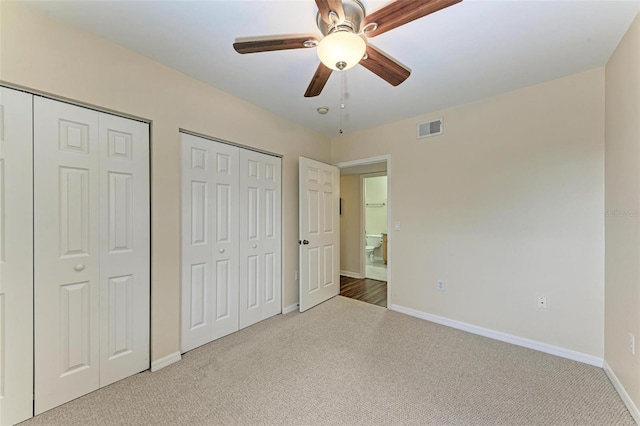 unfurnished bedroom with ceiling fan, light carpet, and multiple closets