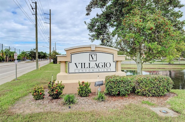 community / neighborhood sign featuring a lawn and a water view