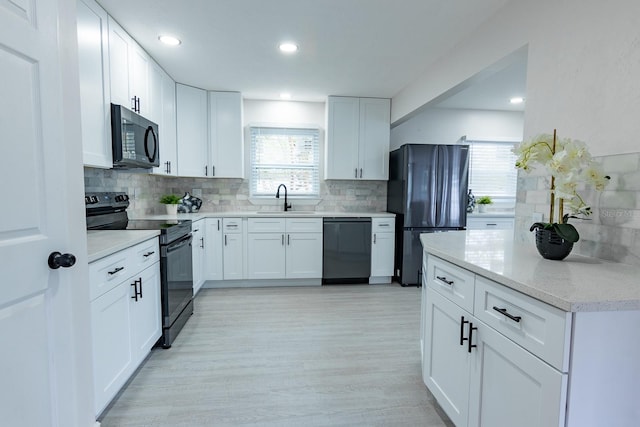 kitchen with backsplash, white cabinets, black appliances, and light hardwood / wood-style floors