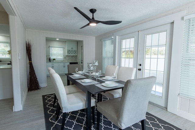 dining space featuring ceiling fan, french doors, crown molding, a textured ceiling, and light wood-type flooring