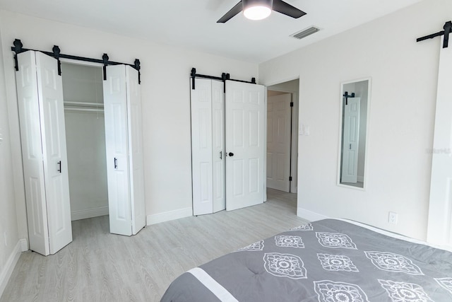 bedroom with ceiling fan, a barn door, and light wood-type flooring