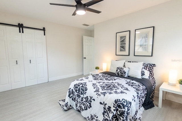 bedroom featuring a barn door, ceiling fan, a closet, and light wood-type flooring