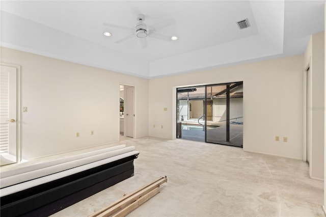 interior space with light carpet, a tray ceiling, and ceiling fan