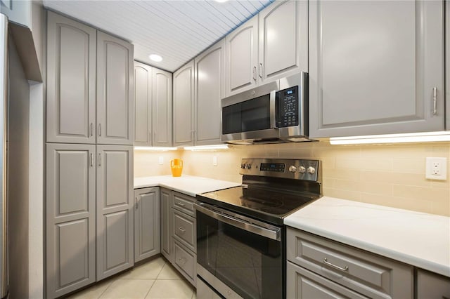 kitchen featuring light stone countertops, stainless steel appliances, gray cabinets, decorative backsplash, and light tile patterned floors