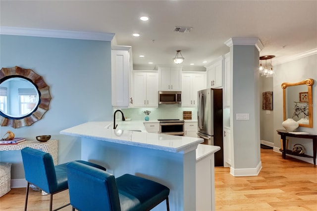 kitchen featuring appliances with stainless steel finishes, sink, pendant lighting, light hardwood / wood-style flooring, and white cabinetry