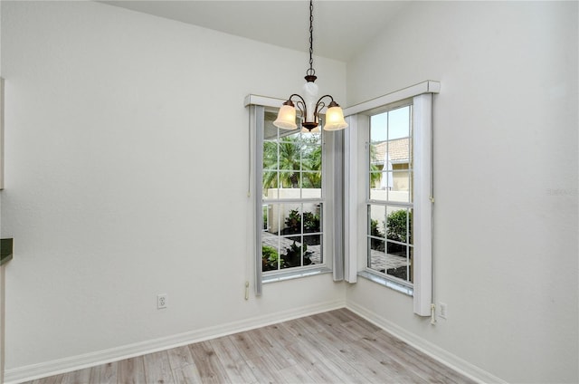 unfurnished dining area featuring light wood-type flooring, vaulted ceiling, and a notable chandelier