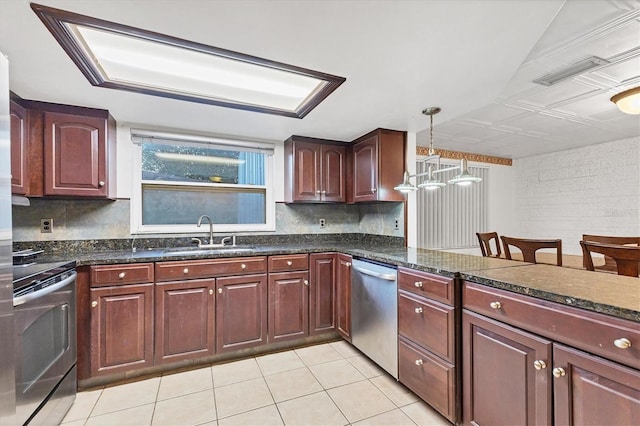 kitchen with dark stone counters, sink, light tile patterned floors, appliances with stainless steel finishes, and decorative light fixtures