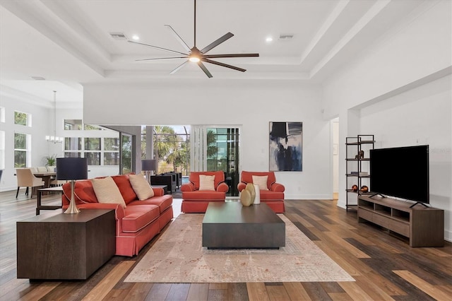 living room with plenty of natural light, wood-type flooring, a high ceiling, and a tray ceiling