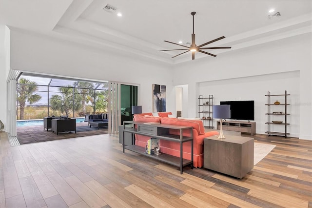 living room featuring a raised ceiling, ceiling fan, a high ceiling, and light wood-type flooring