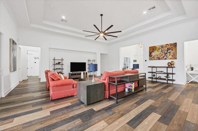 living room featuring a towering ceiling, a tray ceiling, ceiling fan, and dark wood-type flooring