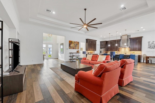 living room with french doors, ceiling fan with notable chandelier, a raised ceiling, and dark wood-type flooring