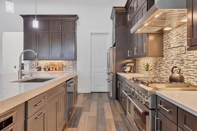 kitchen with sink, wall chimney range hood, dark hardwood / wood-style flooring, decorative light fixtures, and high quality appliances