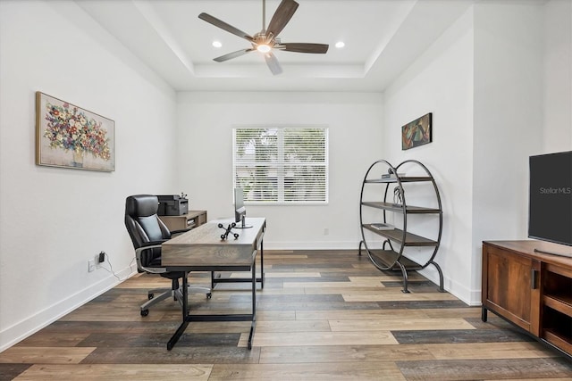 office space featuring dark hardwood / wood-style floors, ceiling fan, and a tray ceiling