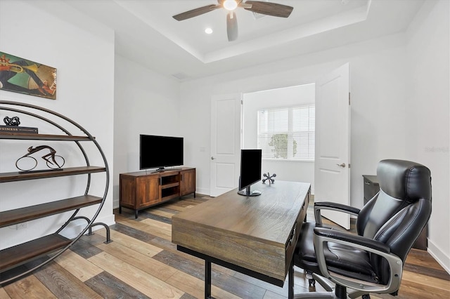 office area featuring ceiling fan, a raised ceiling, and light hardwood / wood-style flooring