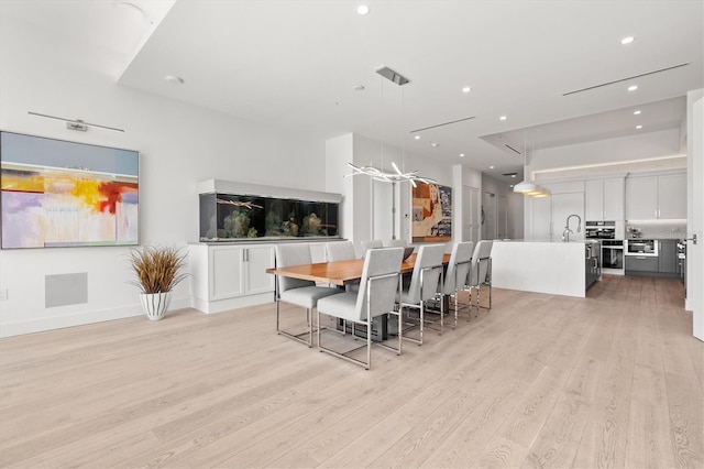 kitchen featuring a center island with sink, white cabinets, pendant lighting, and light hardwood / wood-style flooring