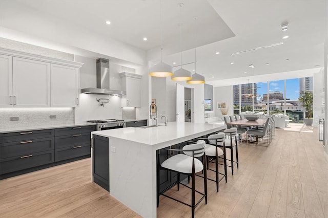 kitchen featuring white cabinets, pendant lighting, wall chimney range hood, and light hardwood / wood-style floors