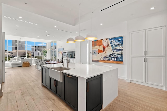 kitchen with pendant lighting, light wood-type flooring, a kitchen island with sink, and sink