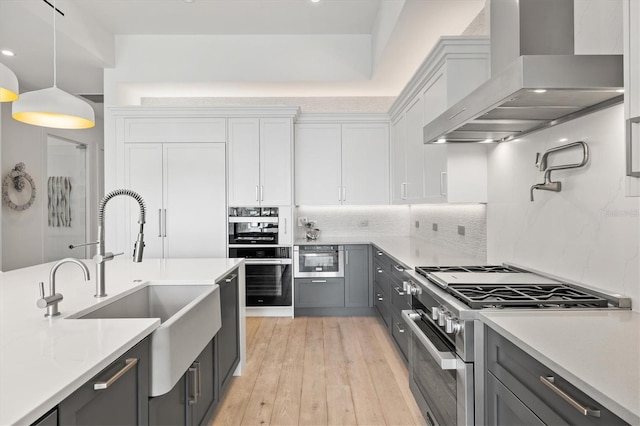 kitchen featuring high end range, light wood-type flooring, wall chimney range hood, decorative light fixtures, and white cabinets