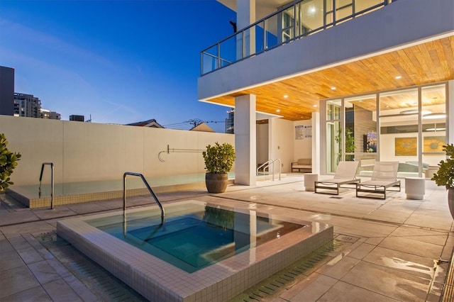 pool at dusk with a patio area and a community hot tub