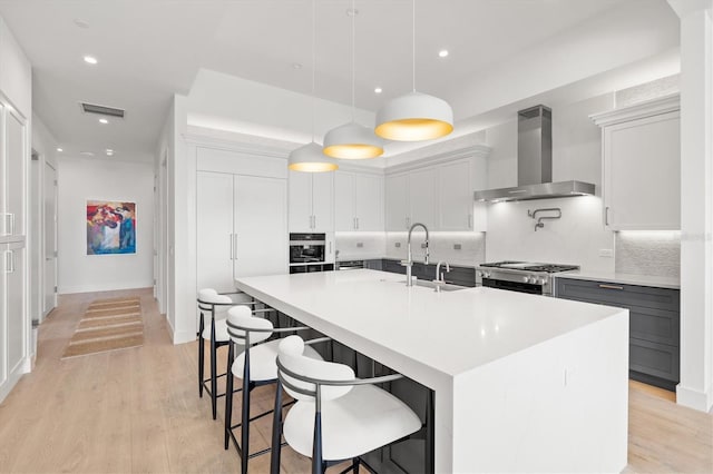 1335 2nd St Unit 301, Sarasota, FL 34236 - kitchen with wall chimney exhaust hood, tasteful backsplash, a center island with sink, light countertops, and light wood-type flooring