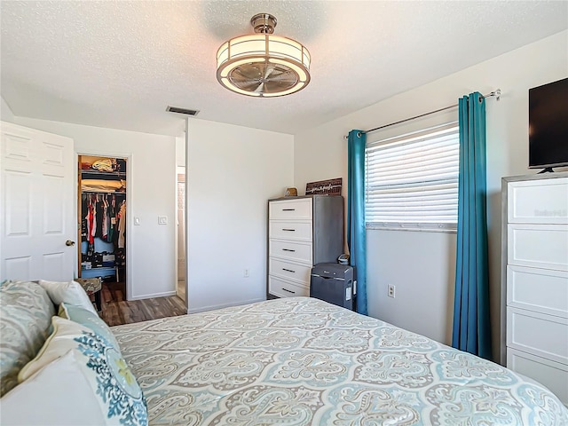 bedroom featuring a spacious closet, a closet, a textured ceiling, and hardwood / wood-style flooring