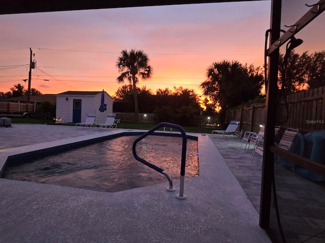 pool at dusk with a patio and a storage unit