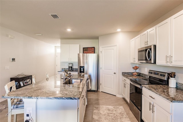 kitchen with dark stone counters, a center island with sink, sink, white cabinetry, and stainless steel appliances