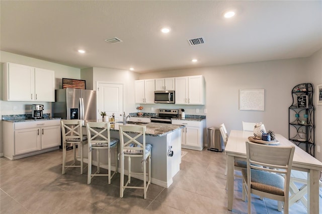 kitchen featuring stone counters, a breakfast bar area, a center island with sink, white cabinets, and appliances with stainless steel finishes