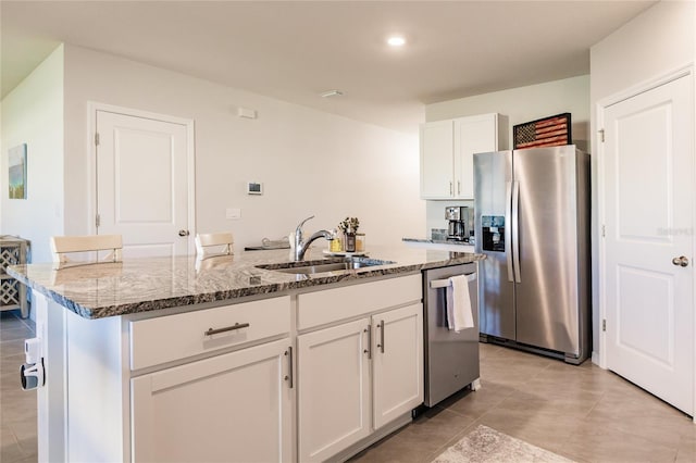 kitchen with white cabinetry, sink, stainless steel appliances, light stone counters, and a center island with sink