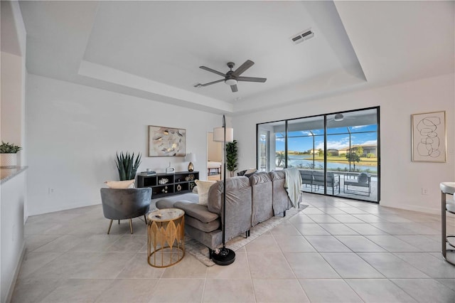 tiled living room featuring ceiling fan, a raised ceiling, and a water view