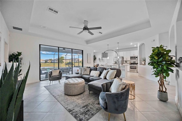 living room with a tray ceiling, ceiling fan, and light tile patterned floors