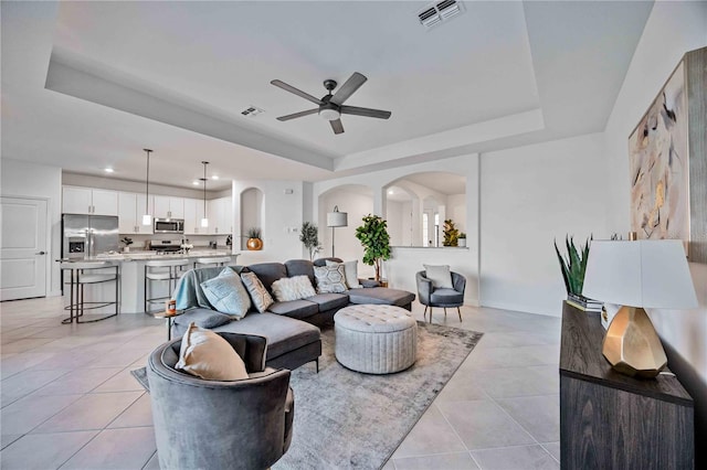 living room featuring ceiling fan, a raised ceiling, and light tile patterned floors