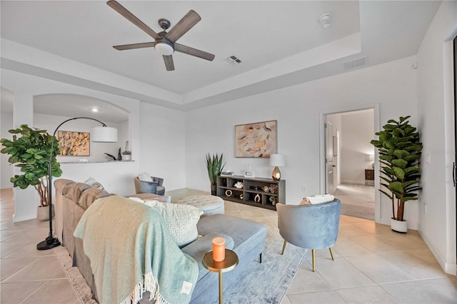 living room with a raised ceiling, ceiling fan, and light tile patterned flooring