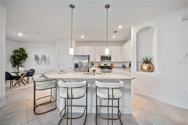 kitchen featuring stainless steel appliances, sink, white cabinetry, hanging light fixtures, and an island with sink