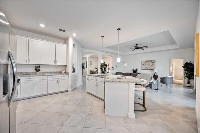 kitchen featuring a tray ceiling, white cabinets, and an island with sink