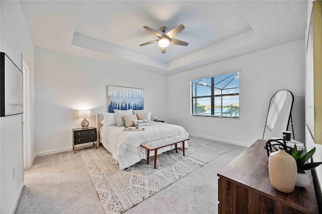 bedroom featuring ceiling fan, light colored carpet, and a tray ceiling