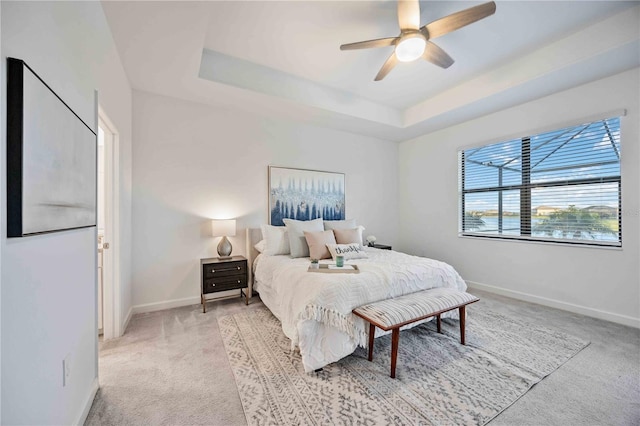 carpeted bedroom with a tray ceiling and ceiling fan