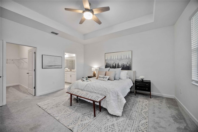 bedroom with a raised ceiling, a walk in closet, ceiling fan, and light colored carpet