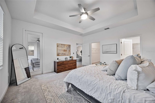 carpeted bedroom with ceiling fan, a closet, a spacious closet, and a tray ceiling